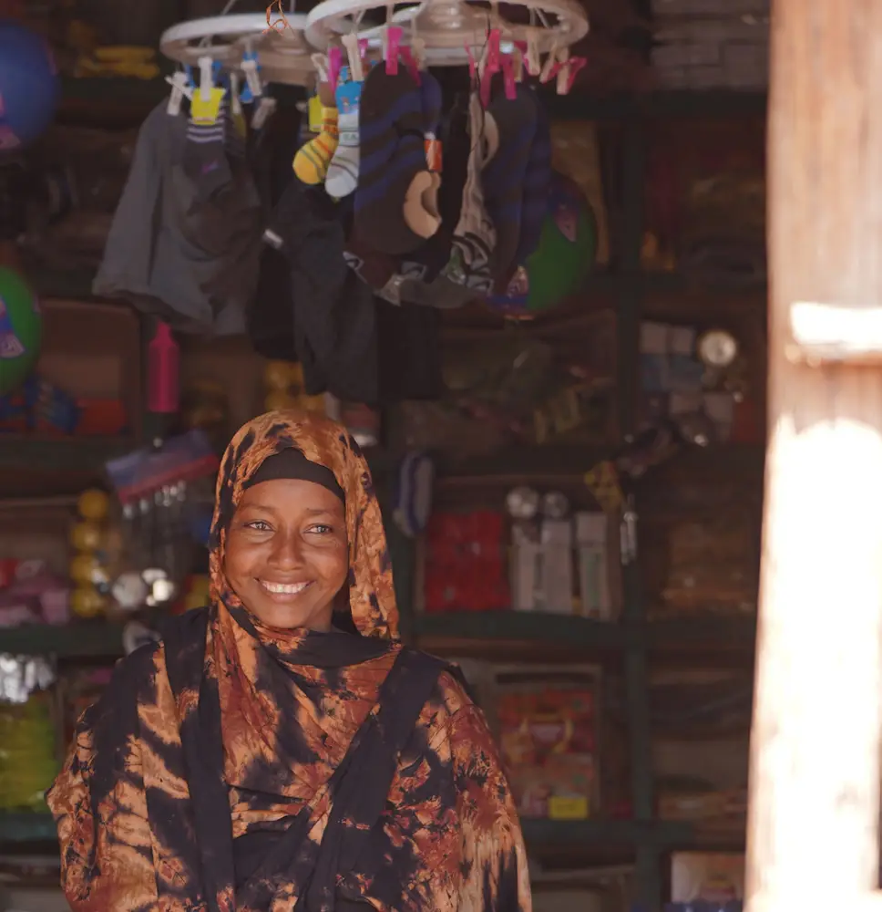 Mrs. Fatuma smiling in her shop, wearing a patterned headscarf.