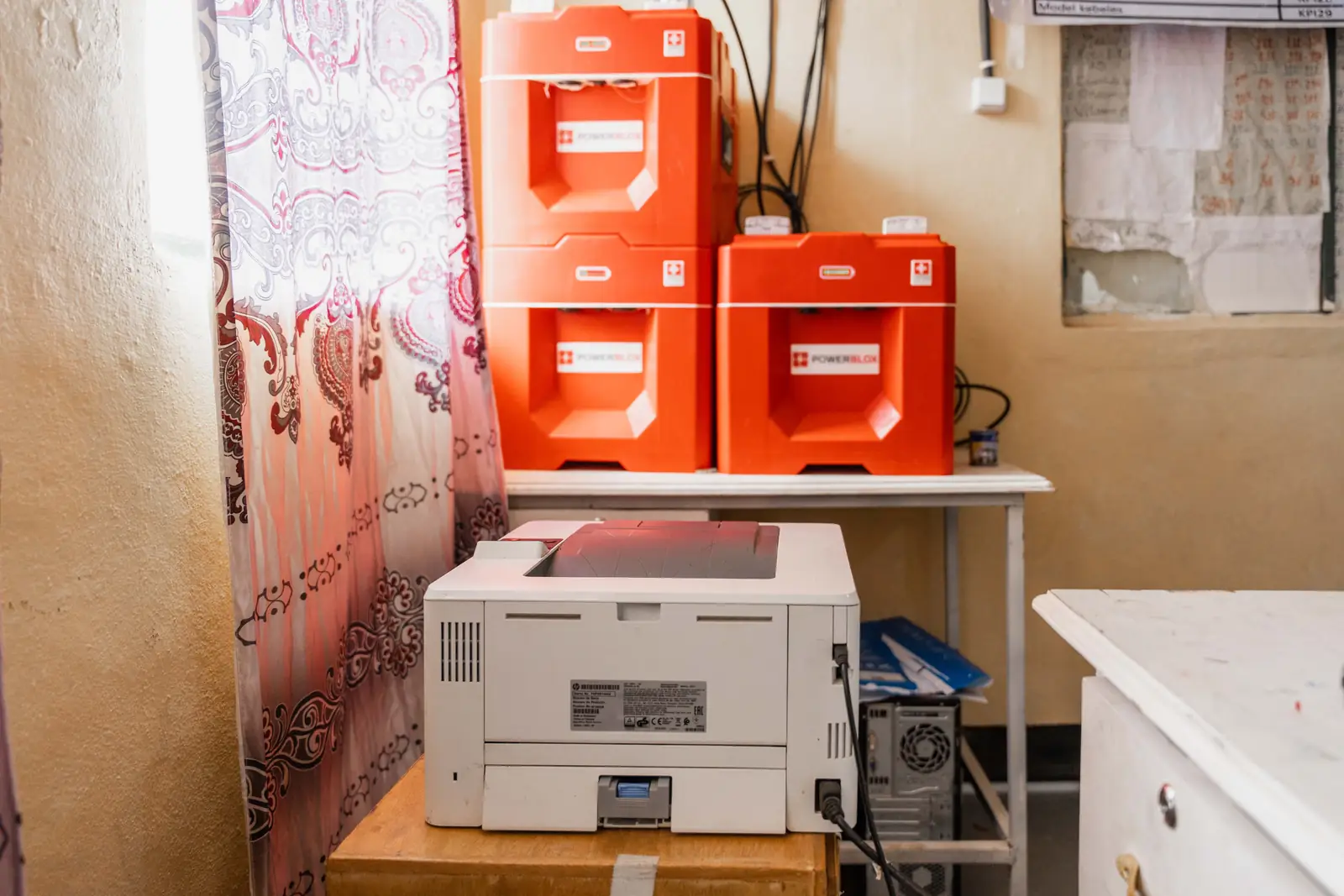 Two stacked red Powerblox units on a desk beside a laser printer in a whitewashed office.