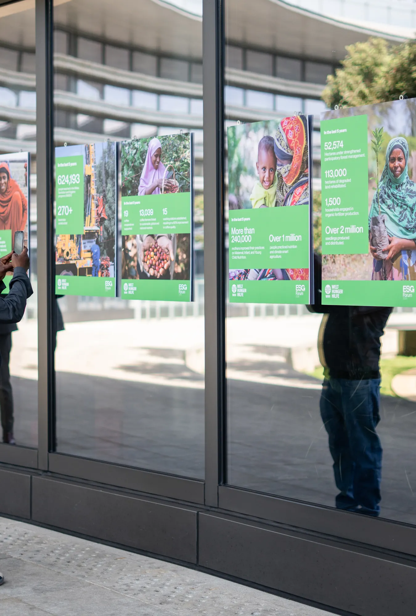 A visitor photographing the exhibition boards along the museum’s glass wall.