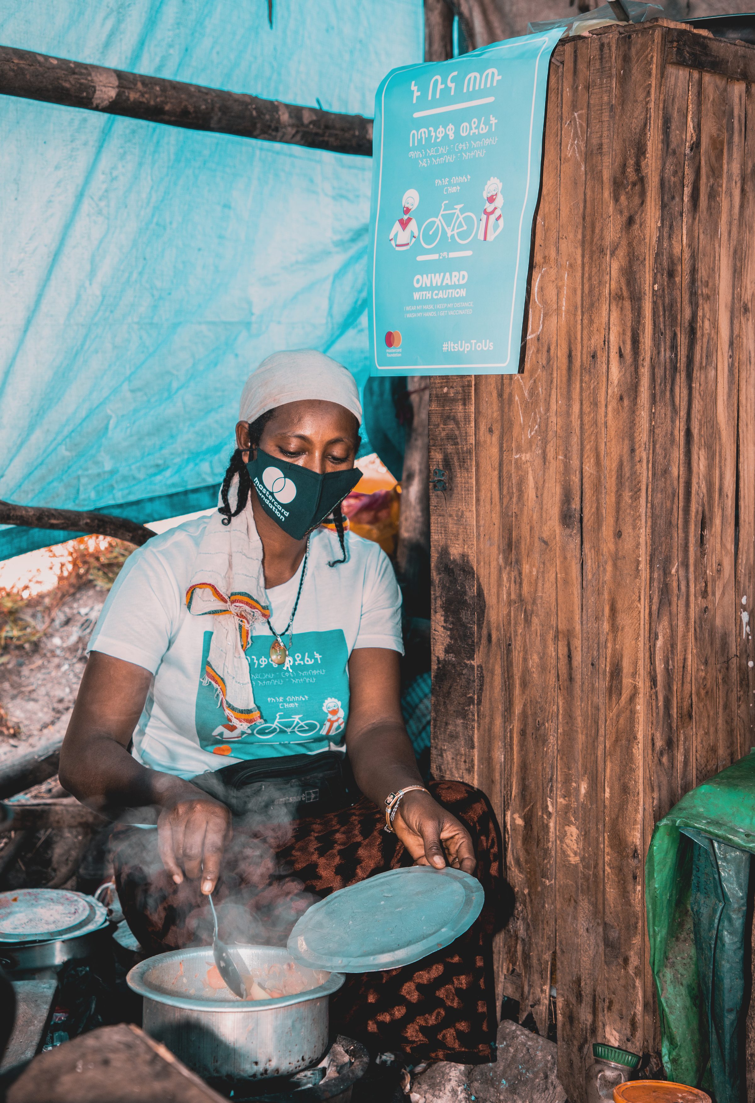 A coffee vendor at her stall preparing coffee, a campaign banner on the wall behind her.