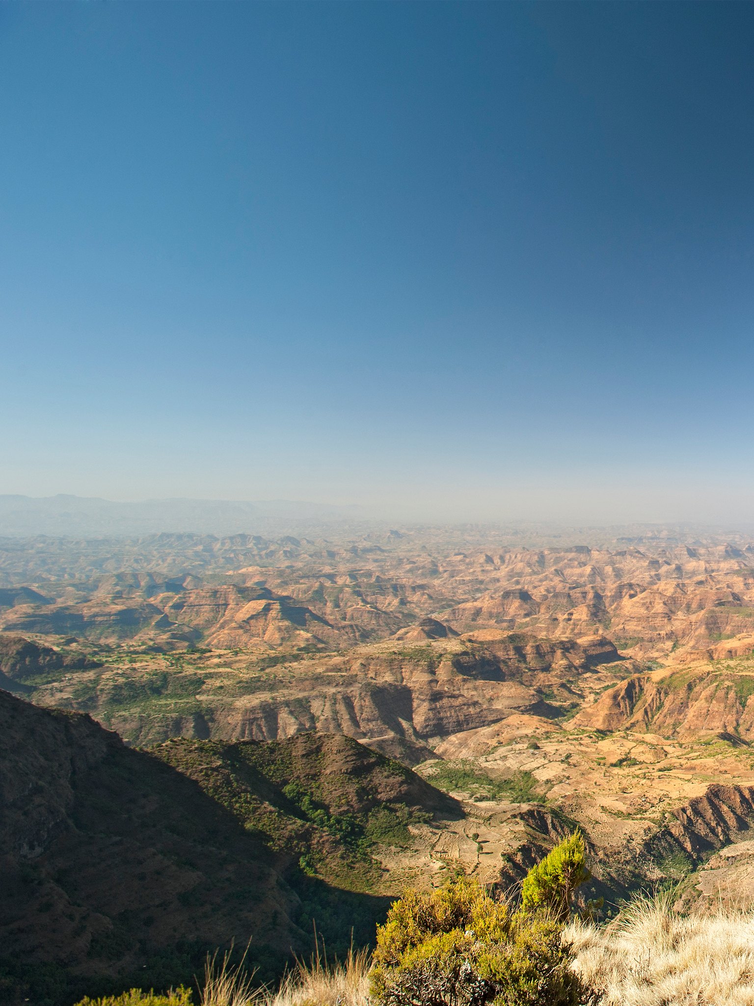 A wide view across the Ethiopian highlands falling away to the lowlands under a clear sky.