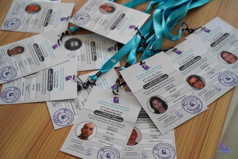 A spread of NEBE accreditation badges for international observers of the 6th General Election, with turquoise lanyards.