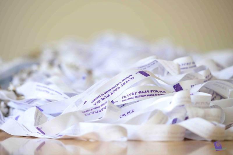A pile of white wristbands printed with the NEBE name in purple, Amharic and English.